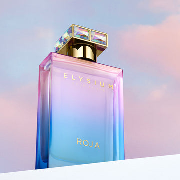 A colorful perfume bottle labeled Elysium Pour Femme ROJA with a gold and iridescent cap, set against a pastel sky background.