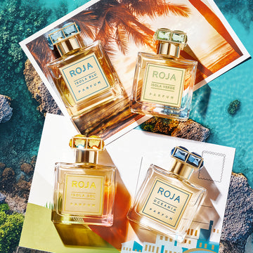 Three bottles of Roja Parfums—Isola Blu, Isola Verde, and Oceania—are arranged on top of tropical postcards, evoking a luxurious, summer vacation atmosphere by the sea.