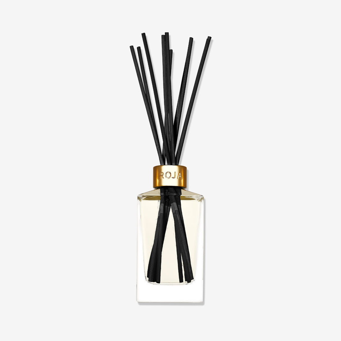 A clear glass reed diffuser bottle with a gold collar, labeled Roja Parfums, holds several black reeds. The light liquid inside features the rich, spicy scent of Amber Aoud by Roja Parfums, set against a plain white background.