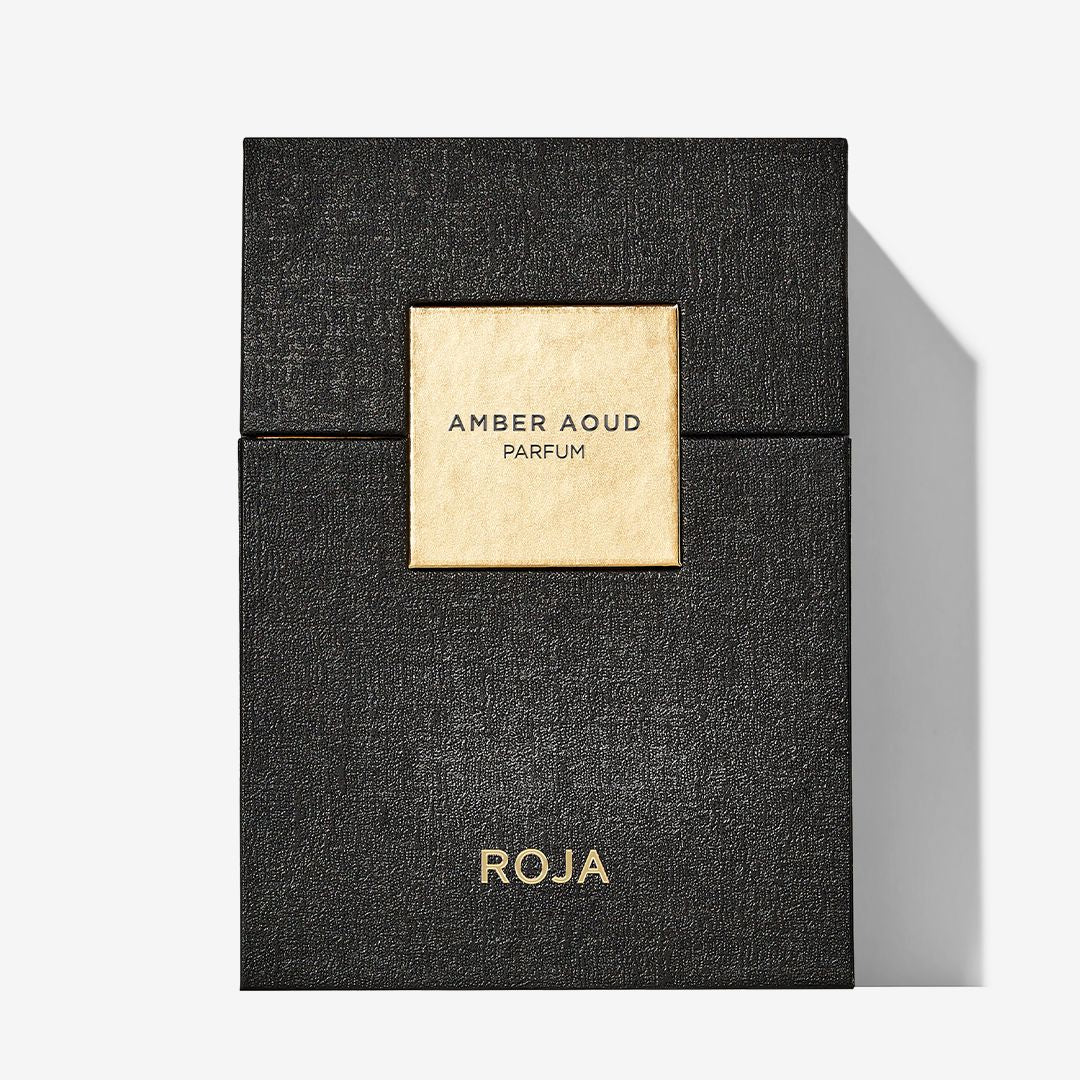 A black textured perfume box with a gold square label reading Amber Aoud and Roja Parfums in gold at the bottom—perfect for oud lovers.