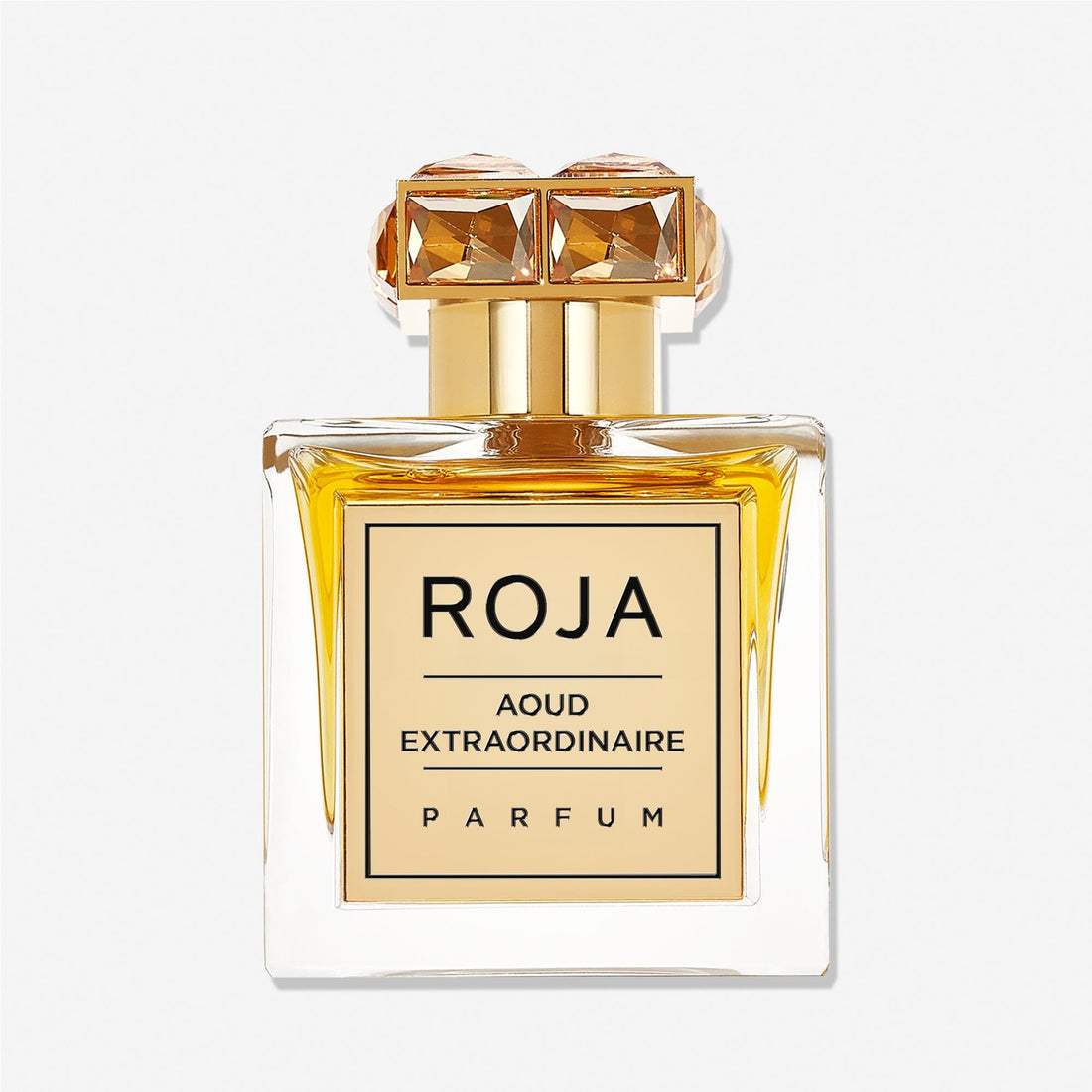 A square glass bottle of Roja Parfums Aoud Extraordinaire holds golden-yellow liquid, featuring a gold gem-accented cap and a front label reading AOUD EXTRAORDINAIRE, capturing the essence of refined oud.