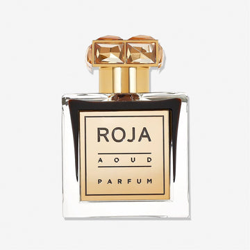 A transparent glass bottle with a gold label reading Roja Parfums Aoud and a gem-like gold rectangular cap displays this luxurious Agarwood perfume against a plain white background.