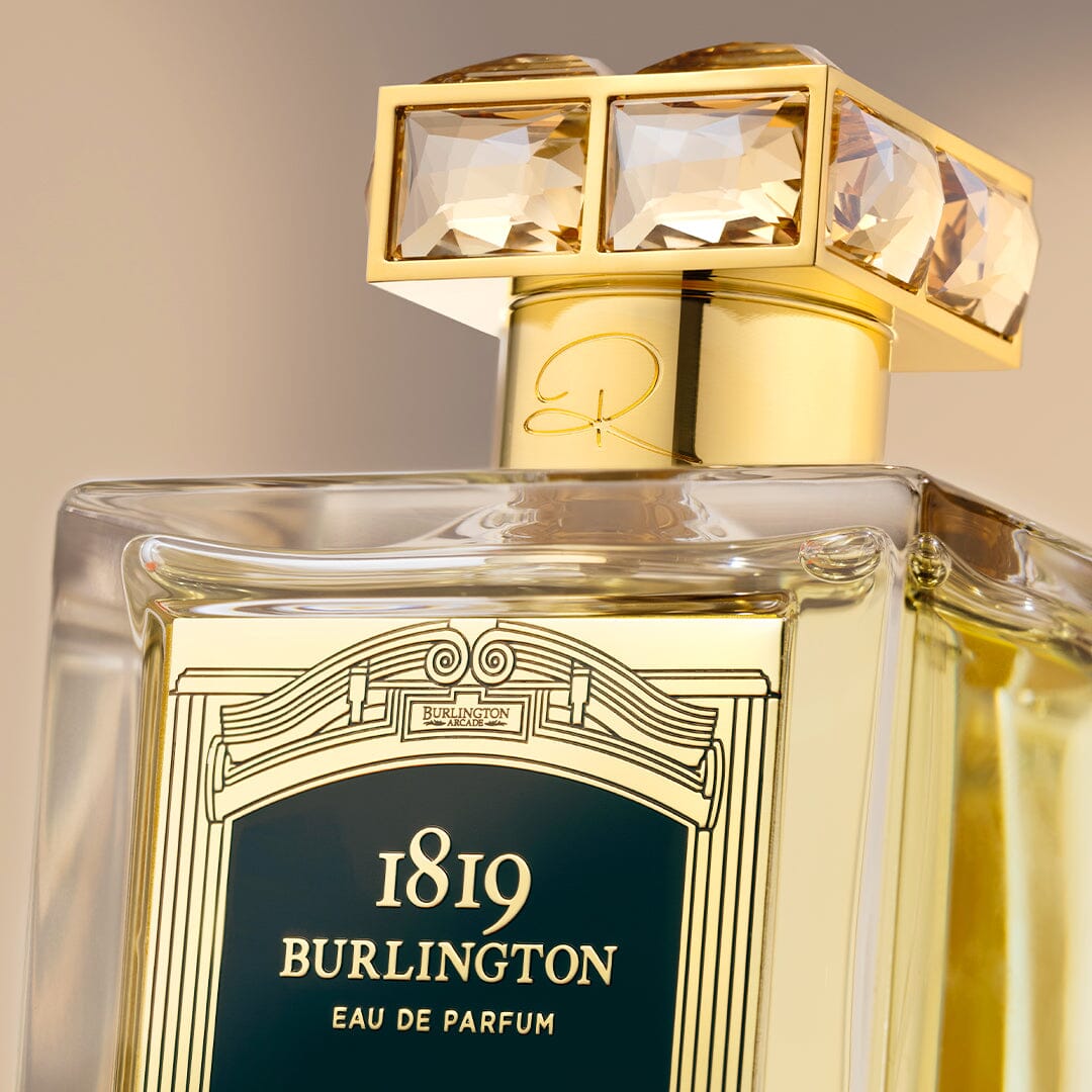 A close-up of a luxe Roja Parfums Burlington 1819 bottle with a gold, gem-adorned cap, set against a softly blurred backdrop at the flagship Roja boutique in Burlington Arcade.