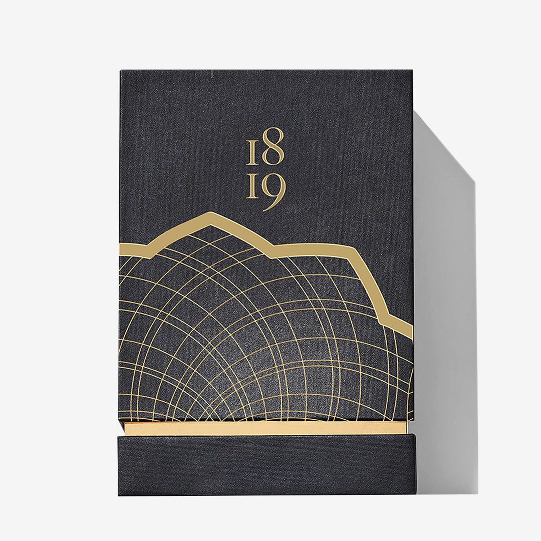 A dark, rectangular box for Roja Parfums’ Burlington 1819 features gold geometric lines, the numbers 18 and 19, and a partial gold-outline mountain or wave design against a plain, light background.