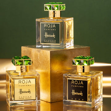 Three bottles of Roja Parfums for Harrods with gold labels and green gemstone caps are displayed on and beside a gold cube against a green and gold background.