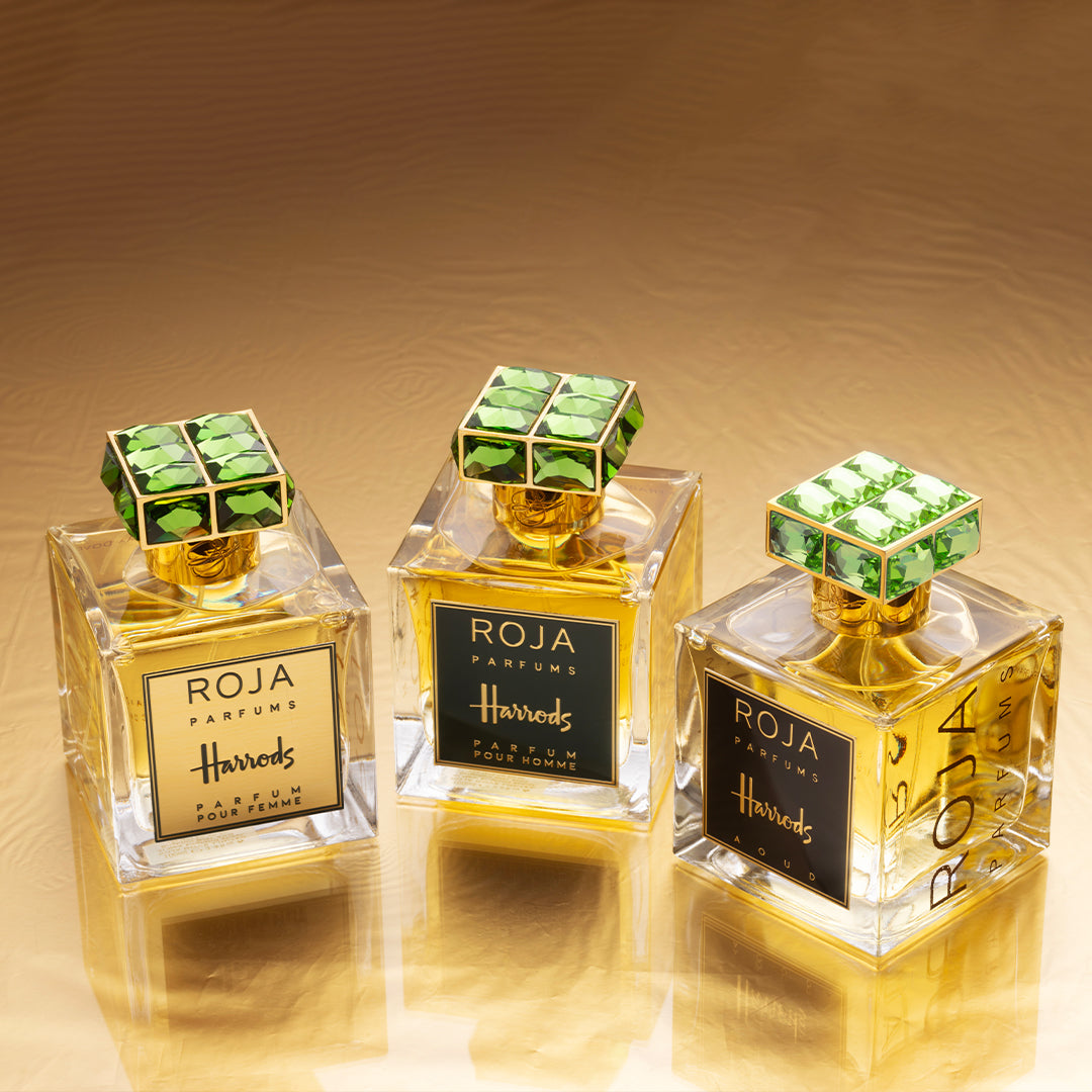 Three elegant Roja Parfums perfume bottles with gold accents and green gem-like caps are displayed on a reflective gold surface, labeled Harrods and positioned closely side by side.
