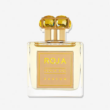 A clear glass perfume bottle labeled Isola Sol by Roja Parfums, topped with a gold cap featuring two large yellow gemstones, evokes island vacation vibes against a plain white background.
