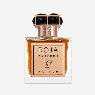 A rectangular glass bottle of Roja Parfums Parfum De La Nuit 2 features amber liquid, a gold label, and a black and gold faceted cap—an elegant choice for lovers of seductive scent, shown against a plain white background.