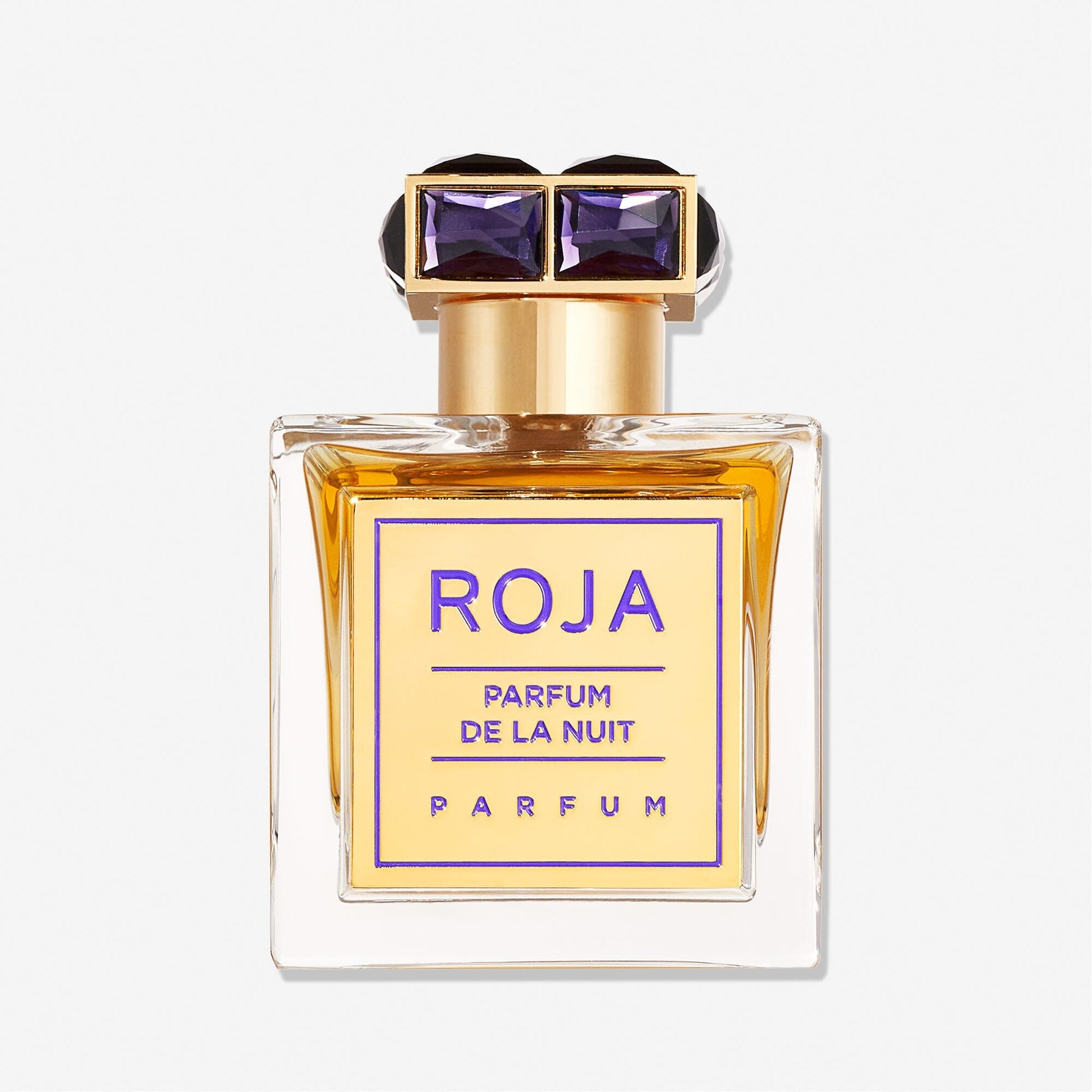 A rectangular bottle of Roja Parfums Parfum De La Nuit displays golden liquid and a gold cap set with two purple gems—a forbidden fragrance that captivates the senses.