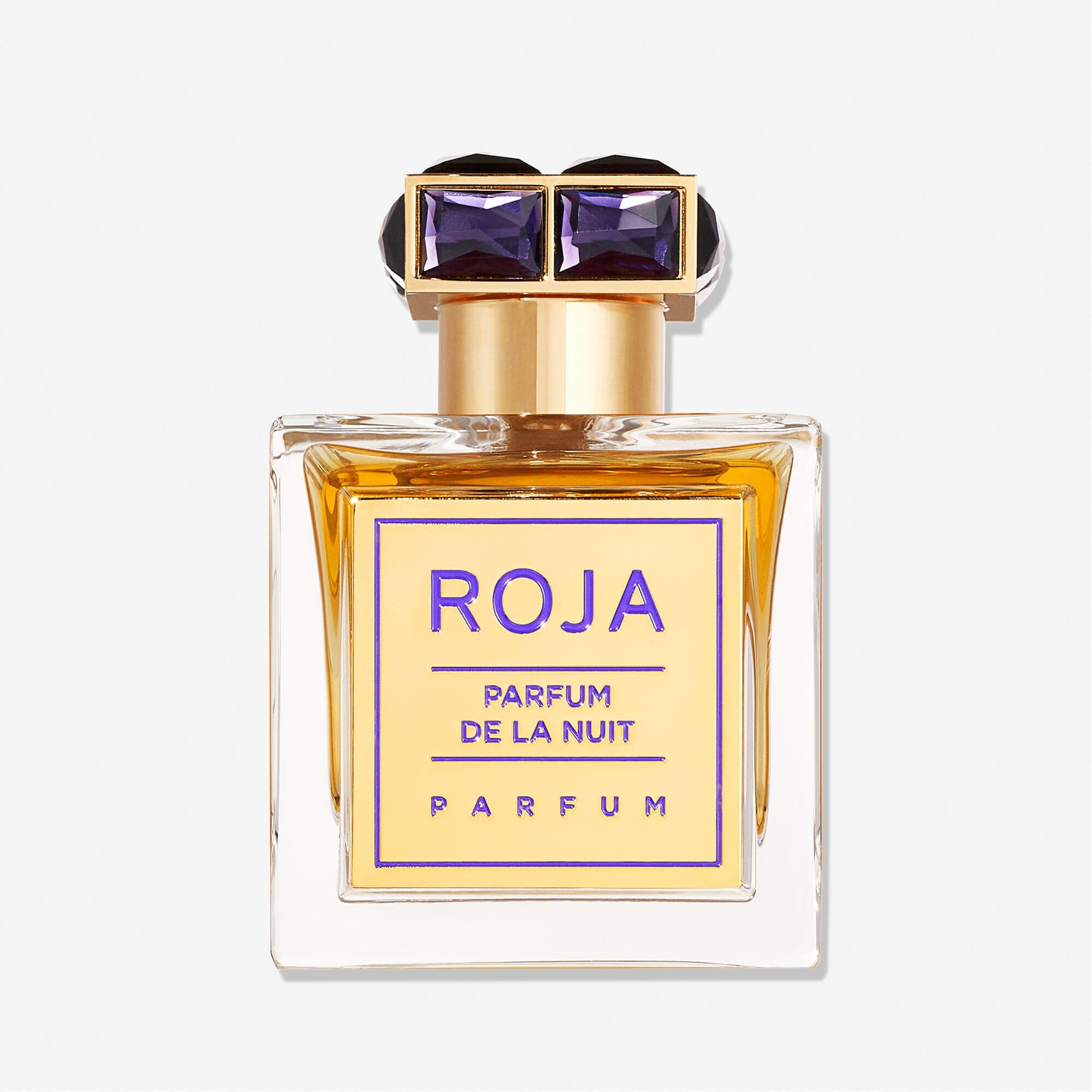 A rectangular bottle of Roja Parfums Parfum De La Nuit displays golden liquid and a gold cap set with two purple gems—a forbidden fragrance that captivates the senses.