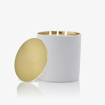 Peony Of Luoyang by Roja Parfums: a white candle with a gold embossed lid and signature logo, glowing with three flames. This exquisite scented candle fills your home with an elegant floral fragrance.