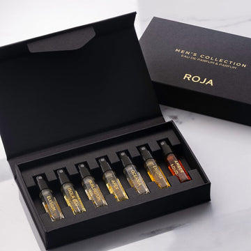 An open black box, The Mens Discovery Collection by Roja Parfums, displays six small fragrances—Elysium, Enigma, Danger, Apex, Oceania, and Amber Aoud—with Men’s Collection Eau de Parfum & Parfum ROJA in gold on the lid.