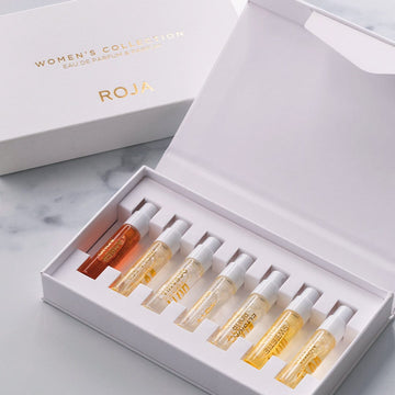 An open white Roja Parfums Womens Discovery Collection box displays eight fragrance sample vials in varying shades, neatly arranged in a row on a marble surface.