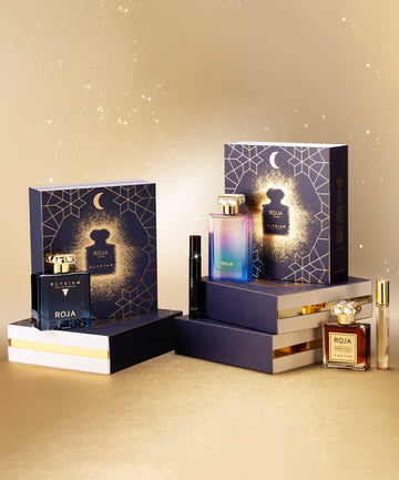Perfume gift sets displayed against a gold, sparkling background. Includes elegant navy boxes with geometric designs and bottles of fragrances in various colors, alongside matching accessories.