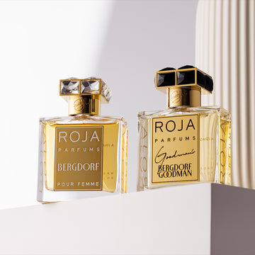 Two elegant perfume bottles with gold labels from Roja Parfums sit on a white ledge; one bottle is labeled Bergdorf Pour Femme, the other Bergdorf Goodman. Soft light creates subtle shadows.