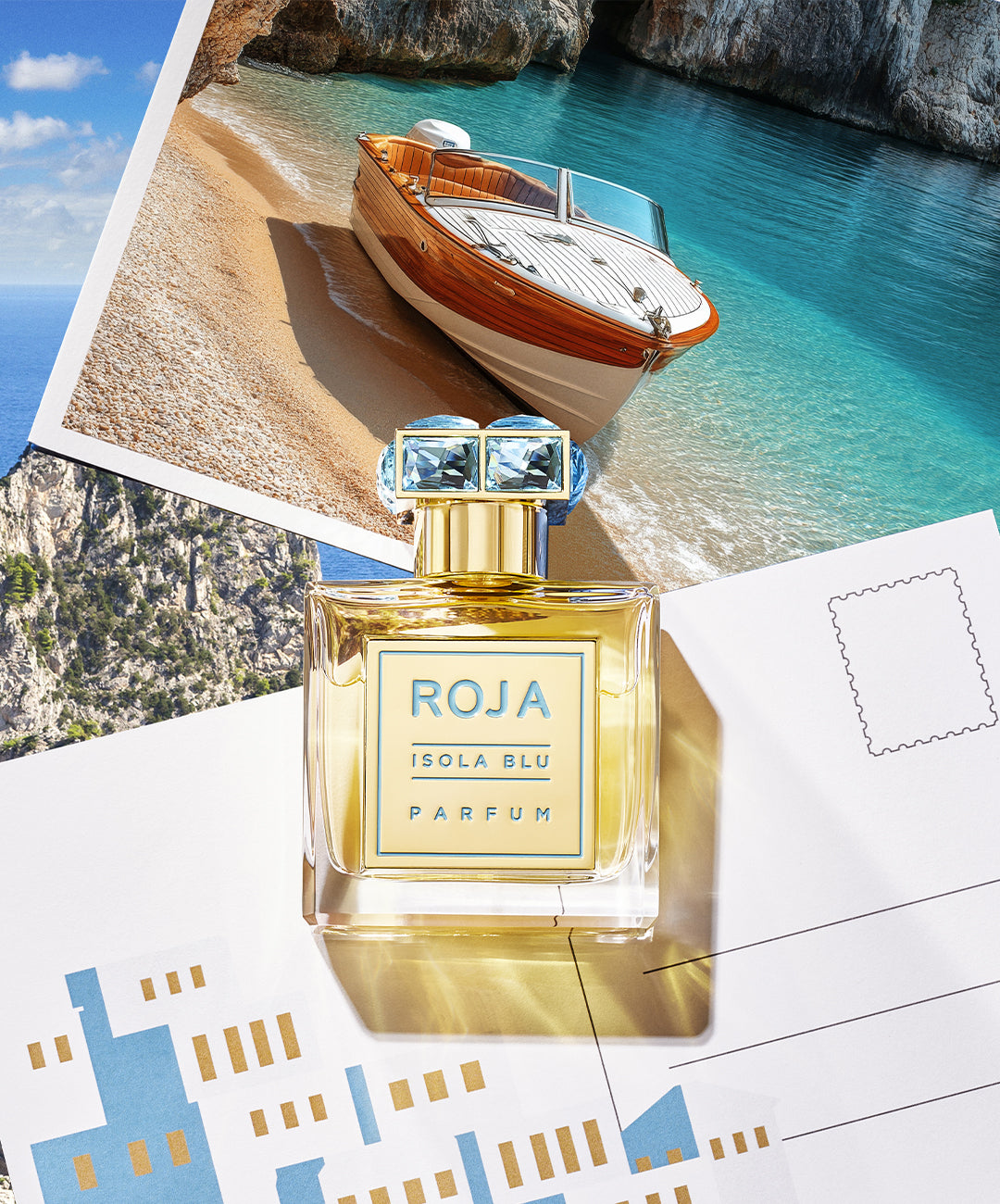 A bottle of Roja Isola Blu Parfum sits on top of travel postcards, one featuring a wooden speedboat on turquoise water by a sandy beach and rocky cliffs, evoking a luxurious, summery seaside vibe.