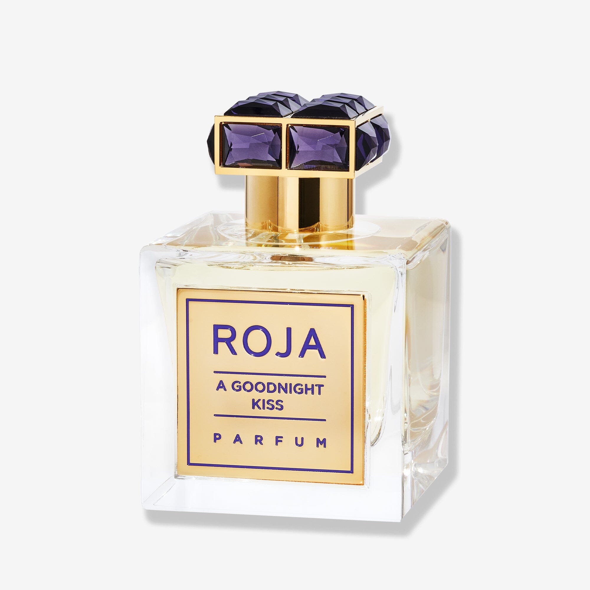 A clear glass bottle labeled "A Goodnight Kiss" by Roja Parfums features a gold and purple cap, capturing a vintage-inspired powdery floral scent, set against a plain white background.