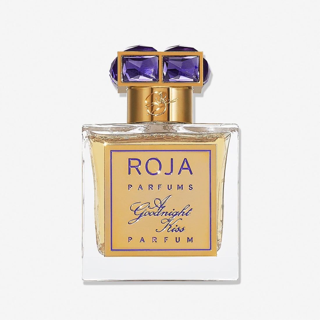 A clear glass bottle of Roja Parfums A Goodnight Kiss, featuring a gold label and an elegant gold cap set with two large purple gemstones.