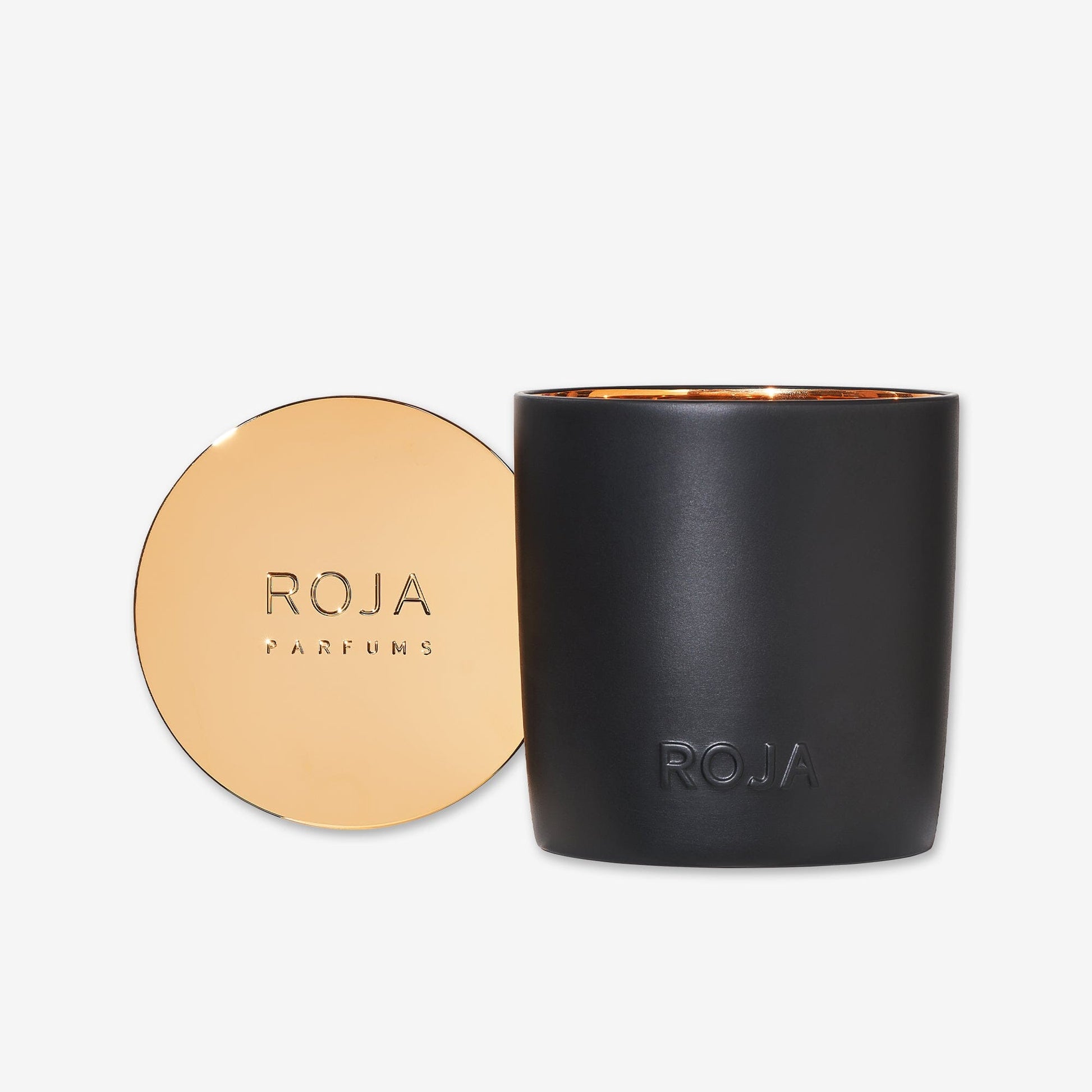 The Amber Aoud scented candle by Roja Parfums comes in a black jar with ROJA embossed on the front and a gold lid engraved with ROJA PARFUMS, set against a minimal white background—an elegant addition to refined interiors.