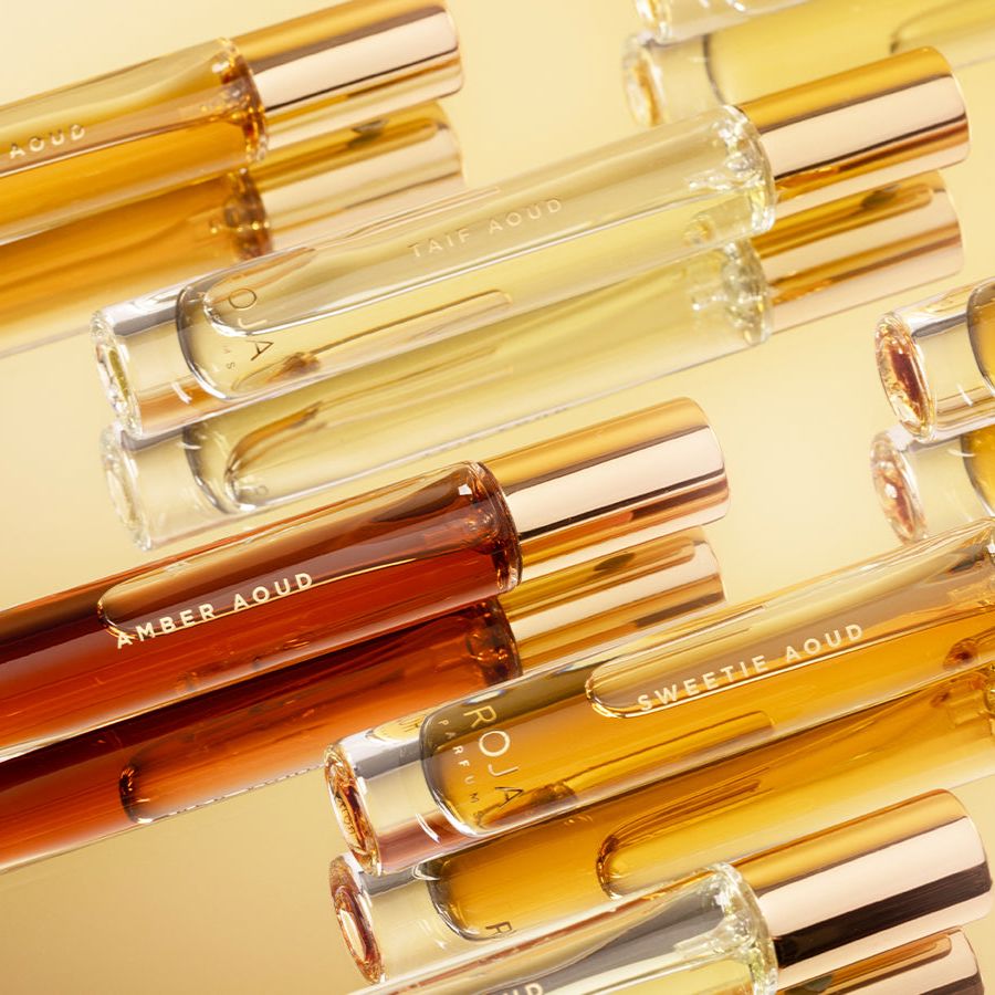 Multiple clear perfume bottles labeled Amber Aoud, Taif Aoud, and Sweetie Aoud with gold caps arranged diagonally on a golden yellow background.