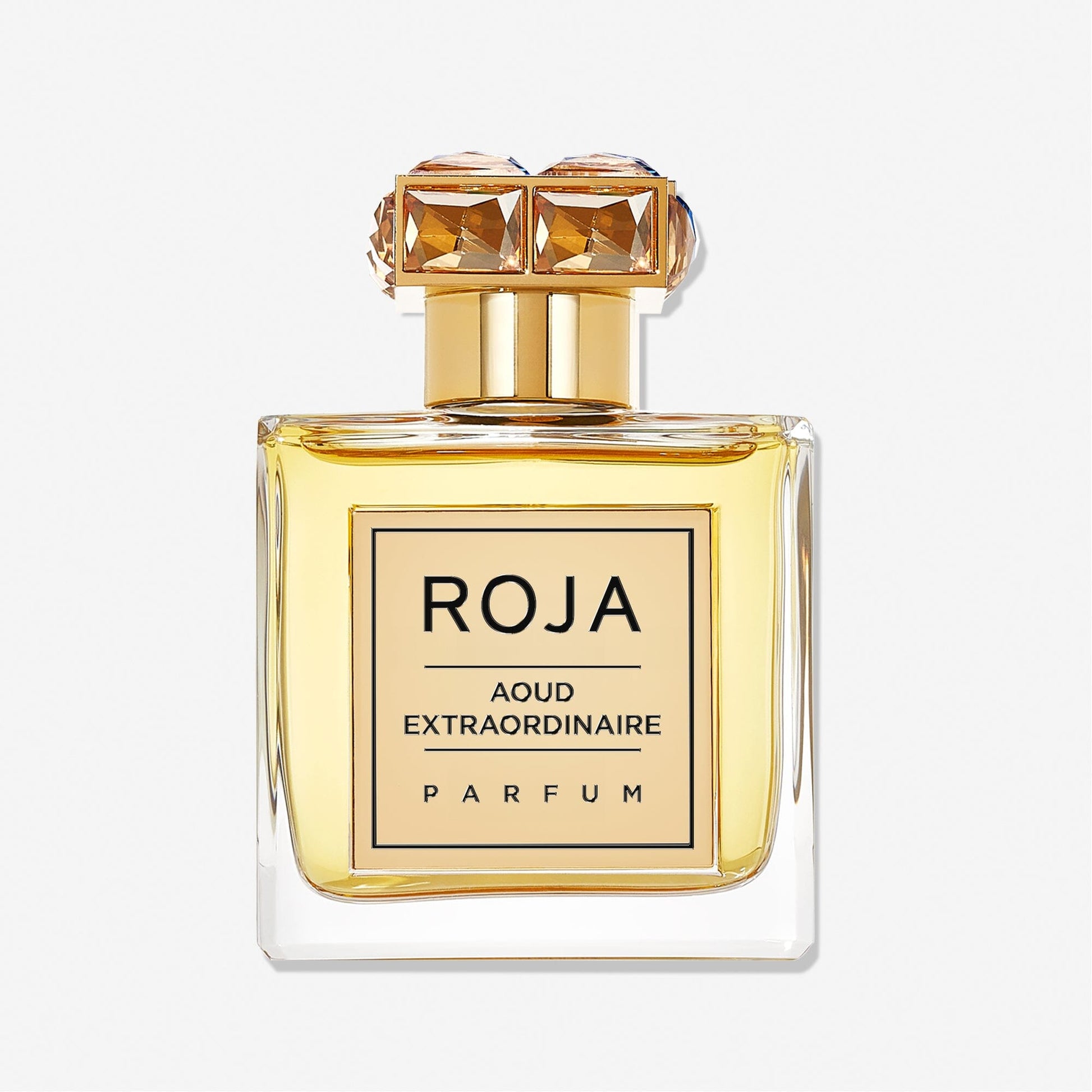 A clear glass bottle of golden liquid labeled Aoud Extraordinaire by Roja Parfums, featuring a gold, jewel-like cap—an elegant luxury fragrance showcased against a white background.