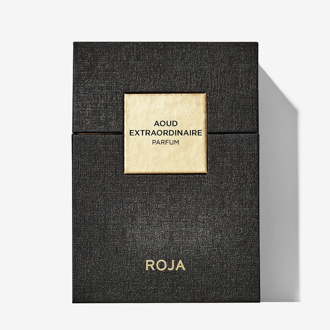 A black textured luxury parfum box with a gold square label reading Aoud Extraordinaire sits centerstage. The brand name Roja Parfums appears in gold at the bottom, and the box casts a shadow to the right—ideal for Oud lovers.