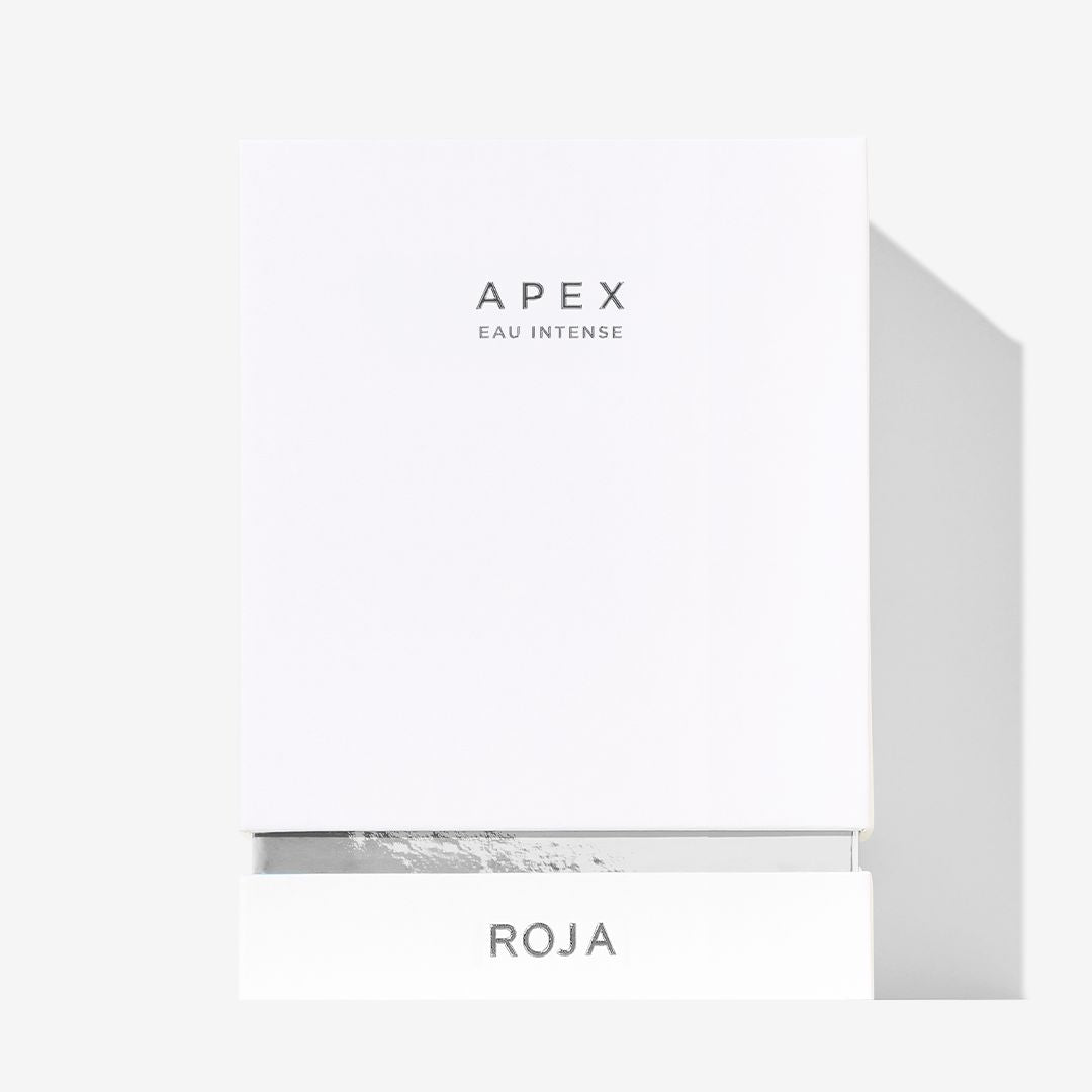 A sleek white box features APEX EAU INTENSE in delicate letters at the center and ROJA PARFUMS boldly at the base, symbolizing refined natural perfumery and a signature Chypré accord. The background is plain and light.