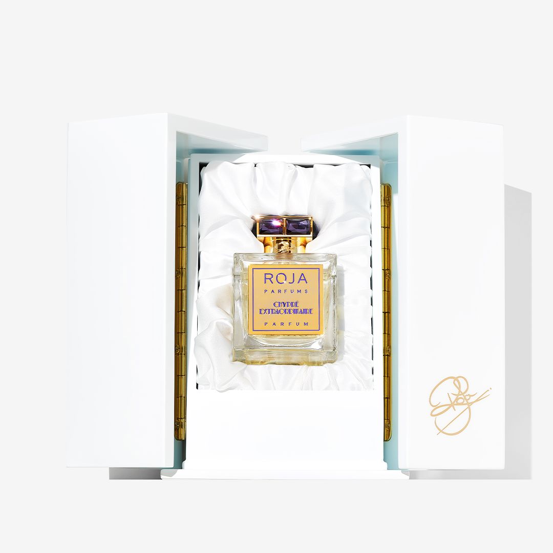 A bottle of Roja Parfums Chypré Extraordinaire is displayed in an open, white, satin-lined luxury box with a gold logo on the lid, suggesting sophisticated bergamot and moss notes inside.