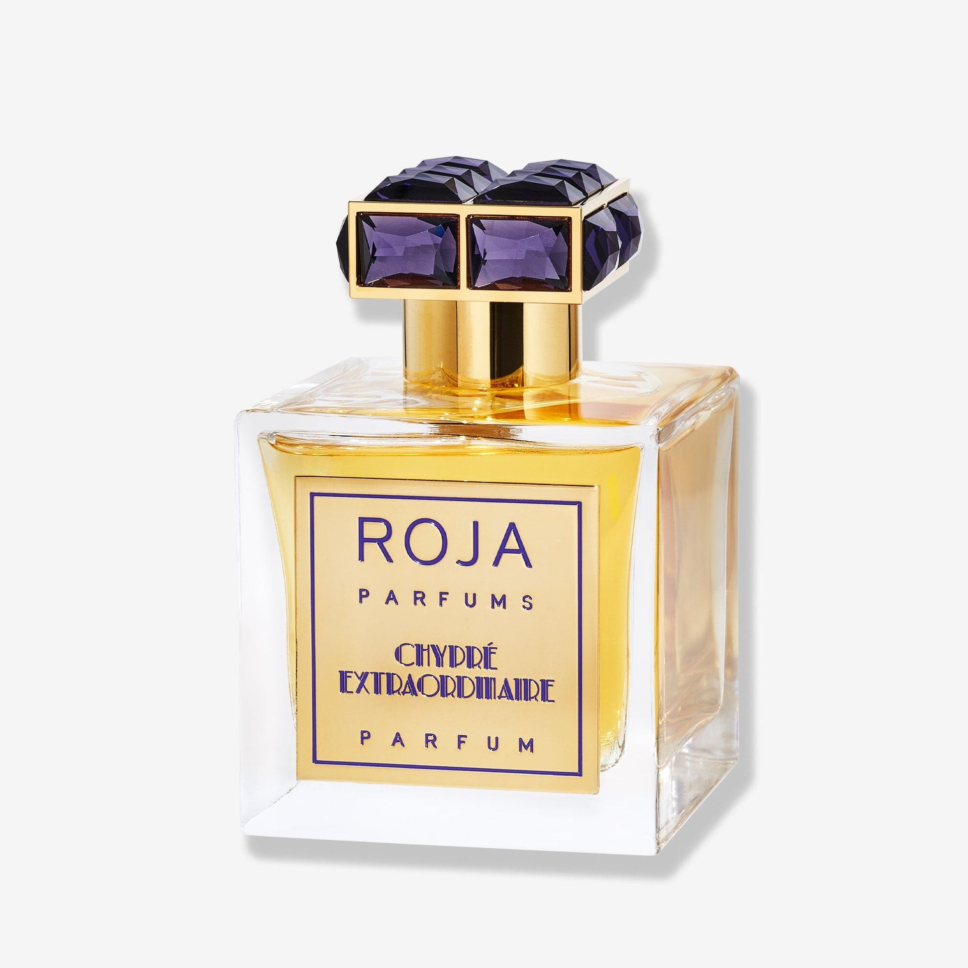 A clear glass bottle labeled "Roja Parfums Chypré Extraordinaire" features a gold cap set with large purple gemstones and holds golden yellow liquid that evokes classic Chypré elegance with refined moss notes.