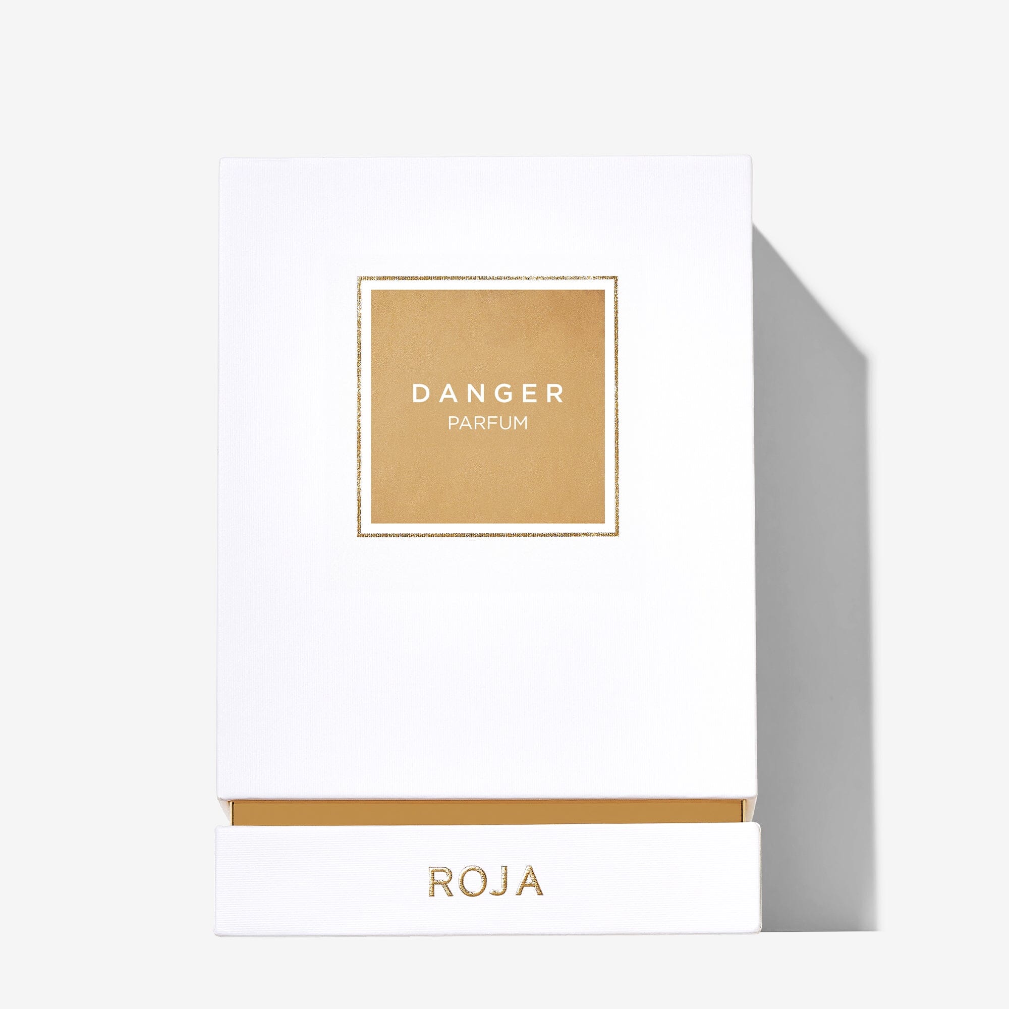 A white rectangular box with a gold square label reading DANGER Pour Femme, ideal for fans of aphrodisiac scents from Roja Parfums. ROJA is displayed in gold uppercase letters at the bottom, and the box casts a shadow to the right.