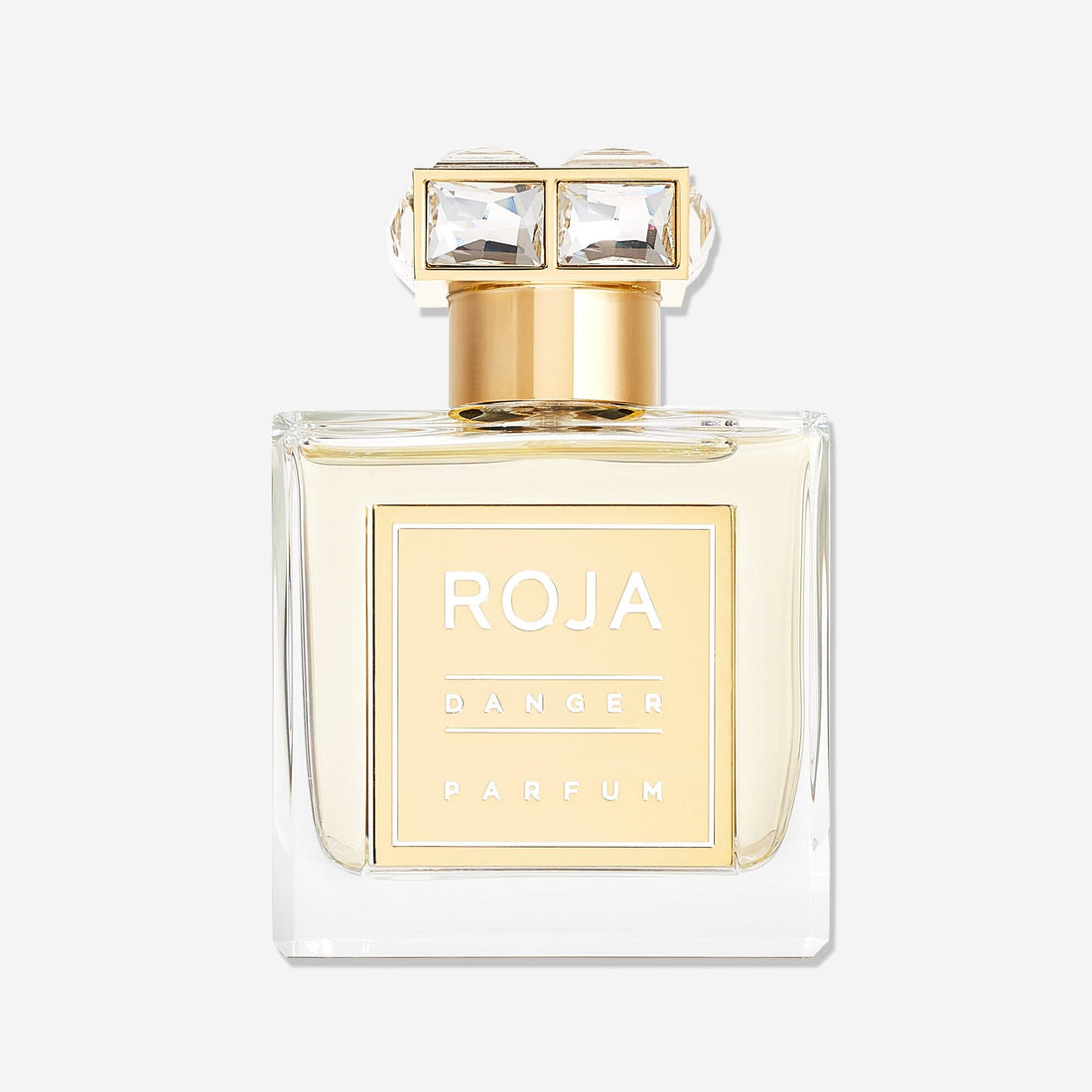 A clear glass bottle of Roja Parfums Danger Pour Femme, featuring a gold label and cap with two large, square-cut gemstones, holds an irresistible aphrodisiac fragrance.