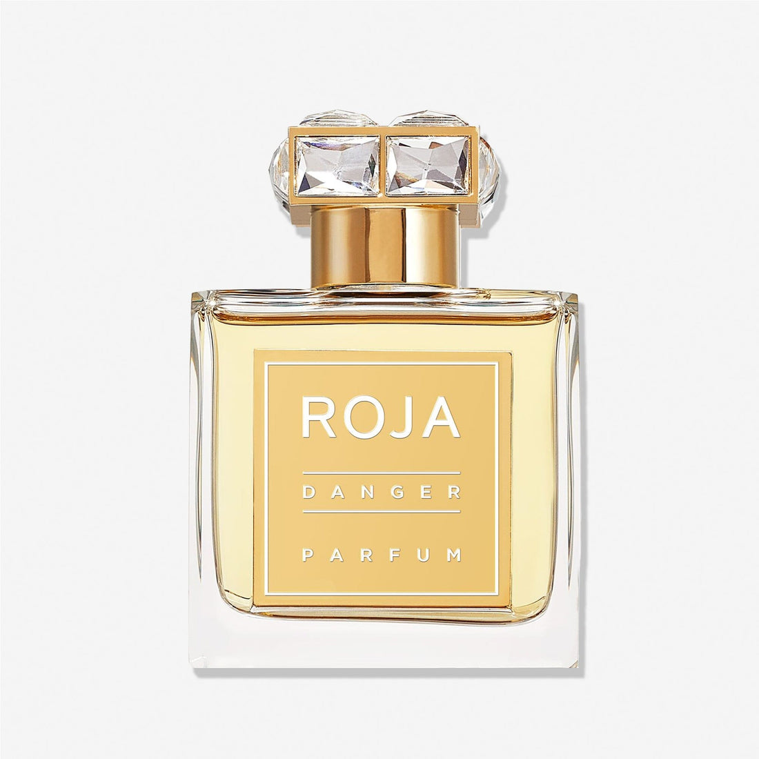 A clear glass bottle of Roja Parfums Danger Pour Femme, featuring a gold label and cap with two gem-like accents. The light amber liquid exudes a femme fatale allure, with hints of Rose de Mai enhancing its elegance.