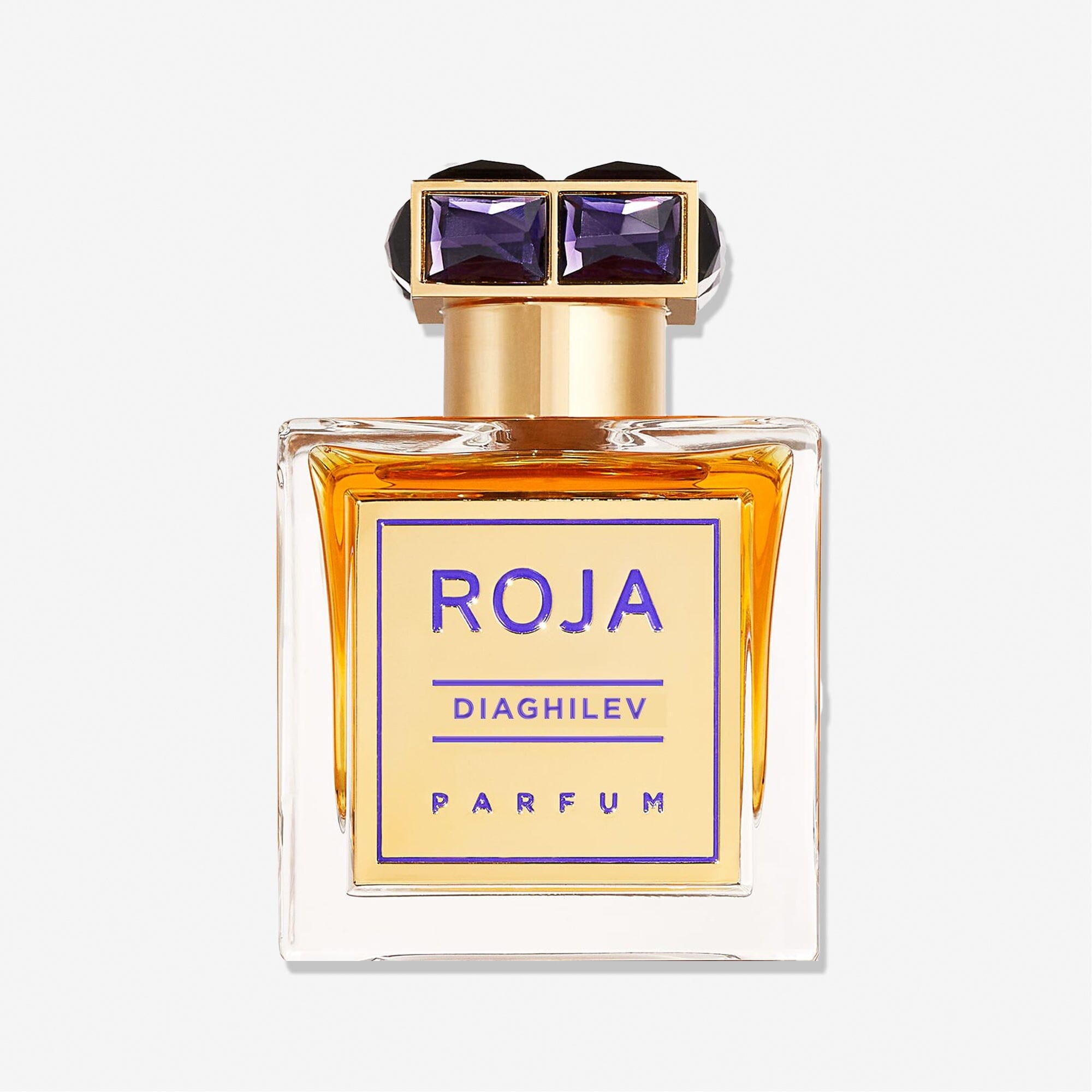A rectangular glass bottle of Diaghilev by Roja Parfums with amber liquid, a gold and purple label, and a gold cap adorned with two purple gem-like accents, highlighting this luxurious Chypré fragrance.