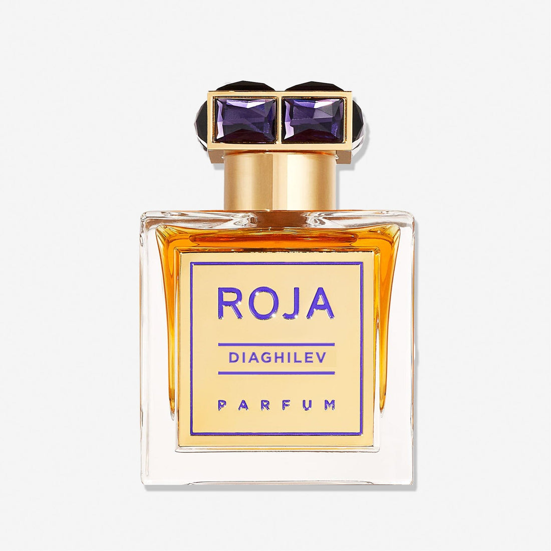 A rectangular glass bottle of Diaghilev by Roja Parfums with amber liquid, a gold and purple label, and a gold cap adorned with two purple gem-like accents, highlighting this luxurious Chypré fragrance.
