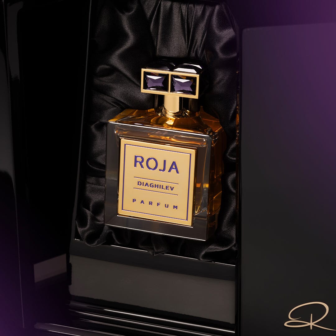 A Roja Parfums Diaghilev bottle, showcasing its Chypré accord, is set against black satin with a gold label and a cap featuring two purple gemstones, embodying an Art-Deco-inspired luxurious and elegant look.
