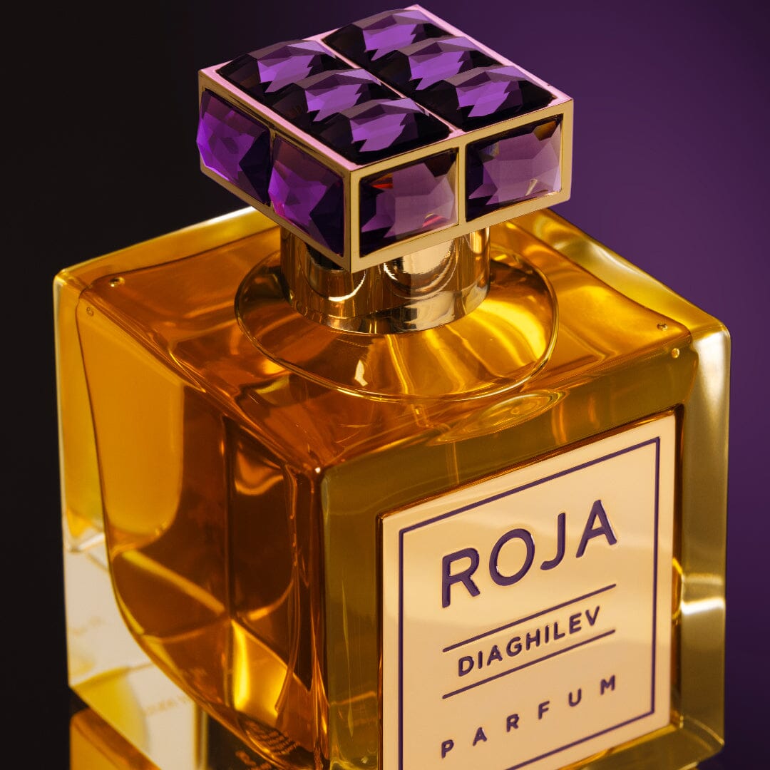 A square, amber-colored bottle with a purple gemstone cap holds Diaghilev by Roja Parfums. The label Roja Diaghilev Parfum stands out on a gradient purple background, capturing the Chypré elegance and Art-Deco nostalgia.