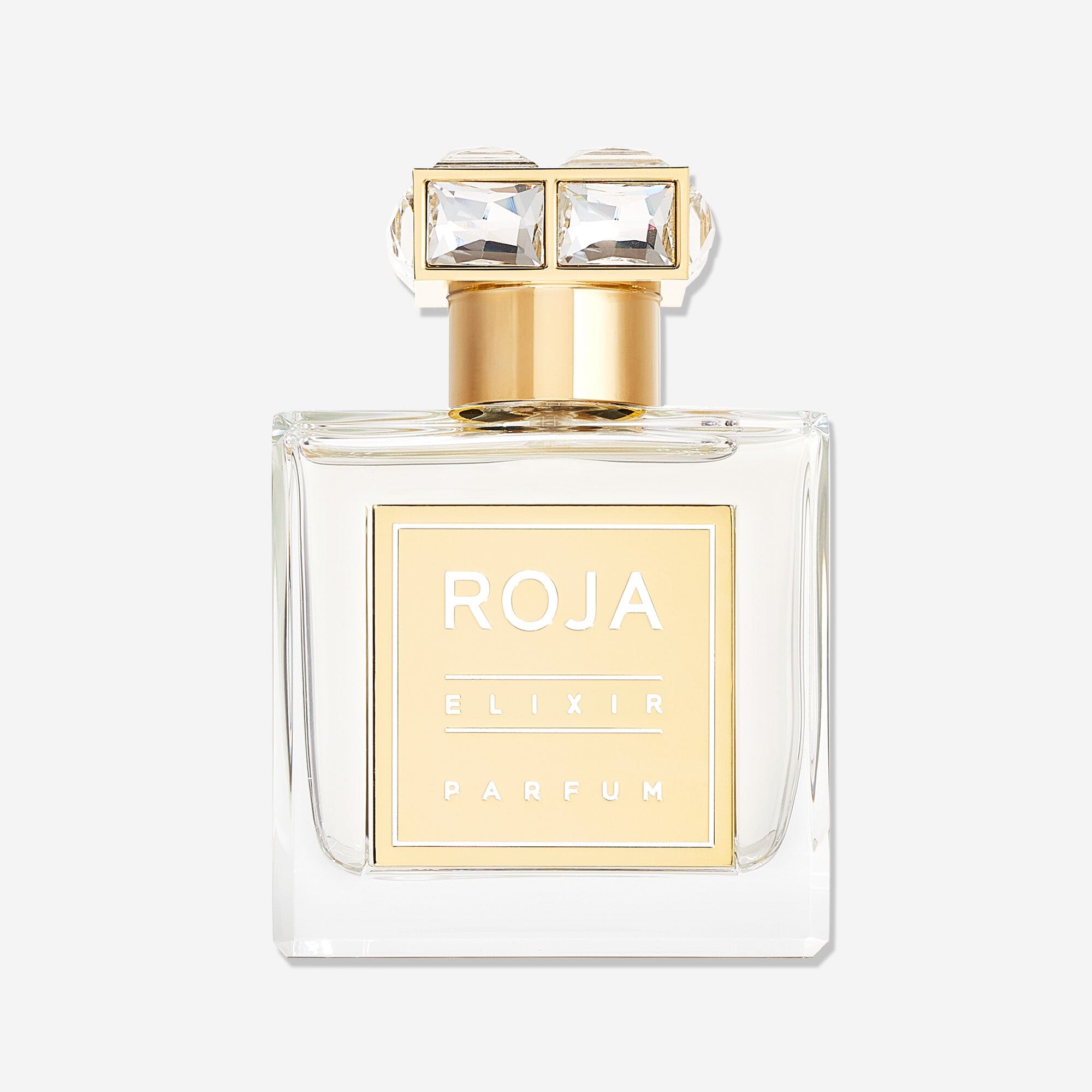 A clear glass bottle of Roja Parfums Elixir Pour Femme with a gold label and cap, topped with two square-cut gemstones, set against a white background—an ethereal fragrance blending vanilla amber musk notes.