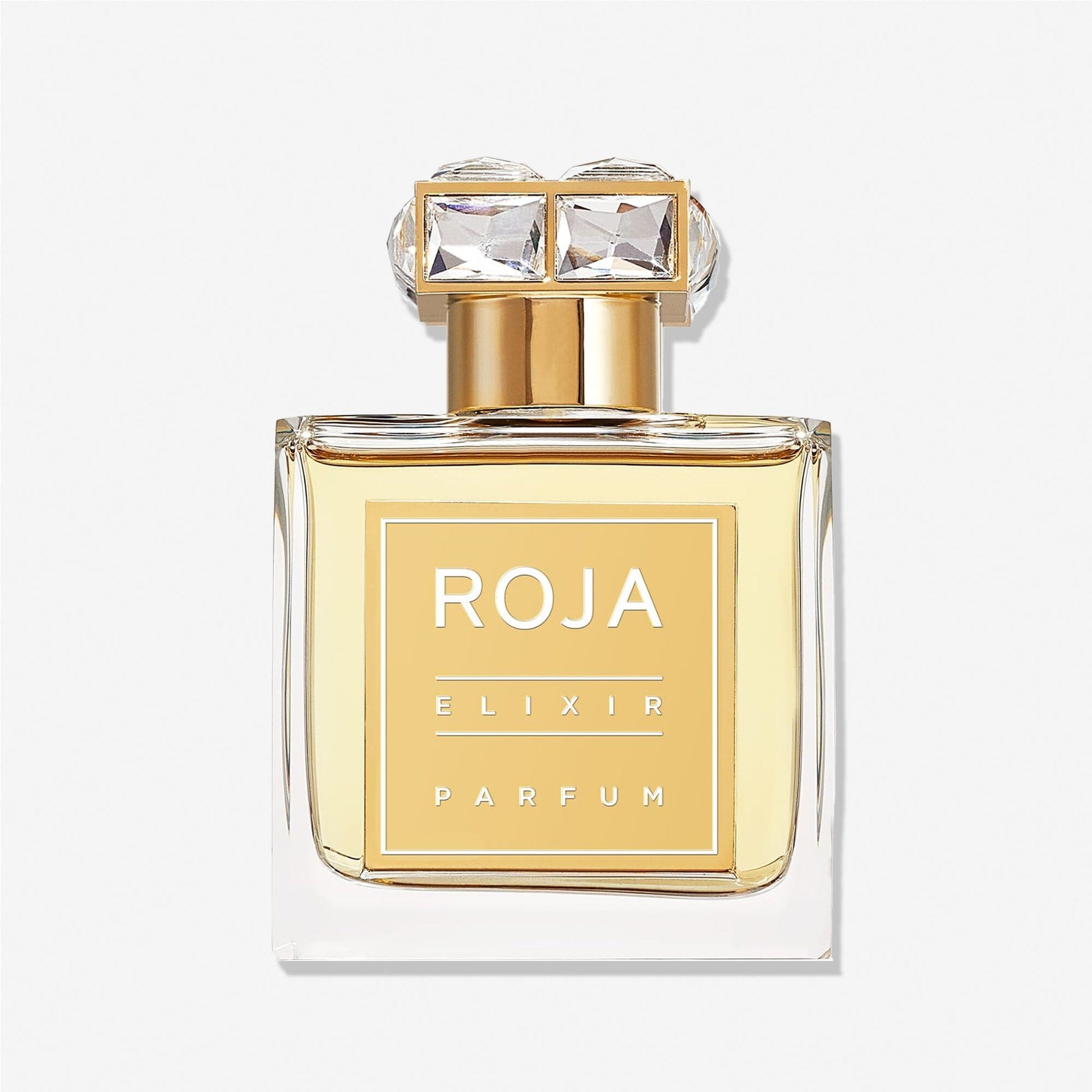 A clear glass bottle of Elixir Pour Femme by Roja Parfums, featuring a gold label and cap with two crystal-like gems, is elegantly photographed against a white background.