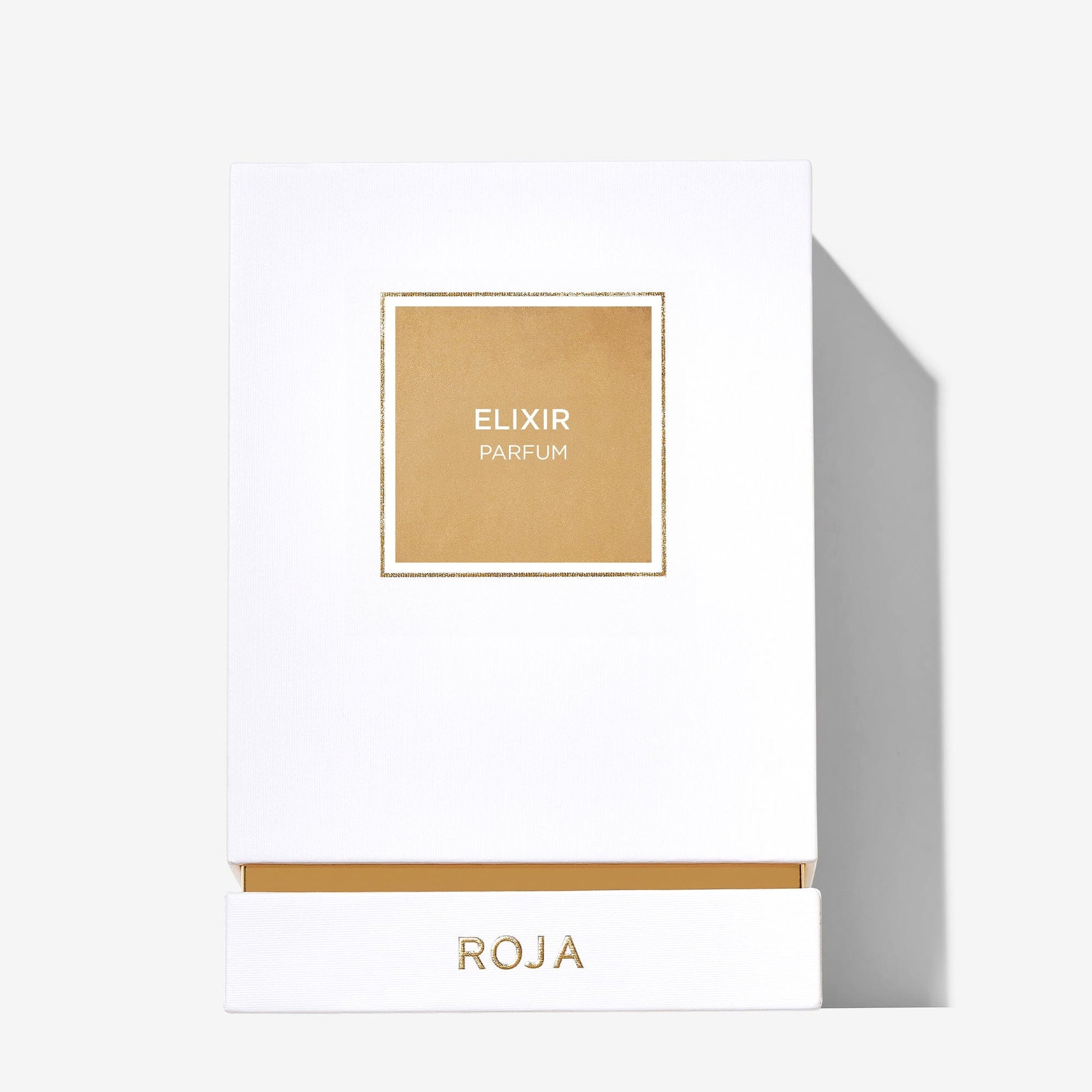 A white box with a gold square label in the center reads Elixir Pour Femme, while Roja Parfums is written in gold at the bottom. The minimalist, elegant design hints at the ethereal fragrance within its jewel-encrusted bottle.