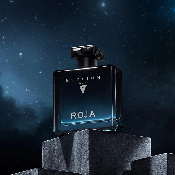 A dark blue glass bottle of Roja Parfums Elysium Noir perfume is shown on stone blocks with a starry night sky in the background.