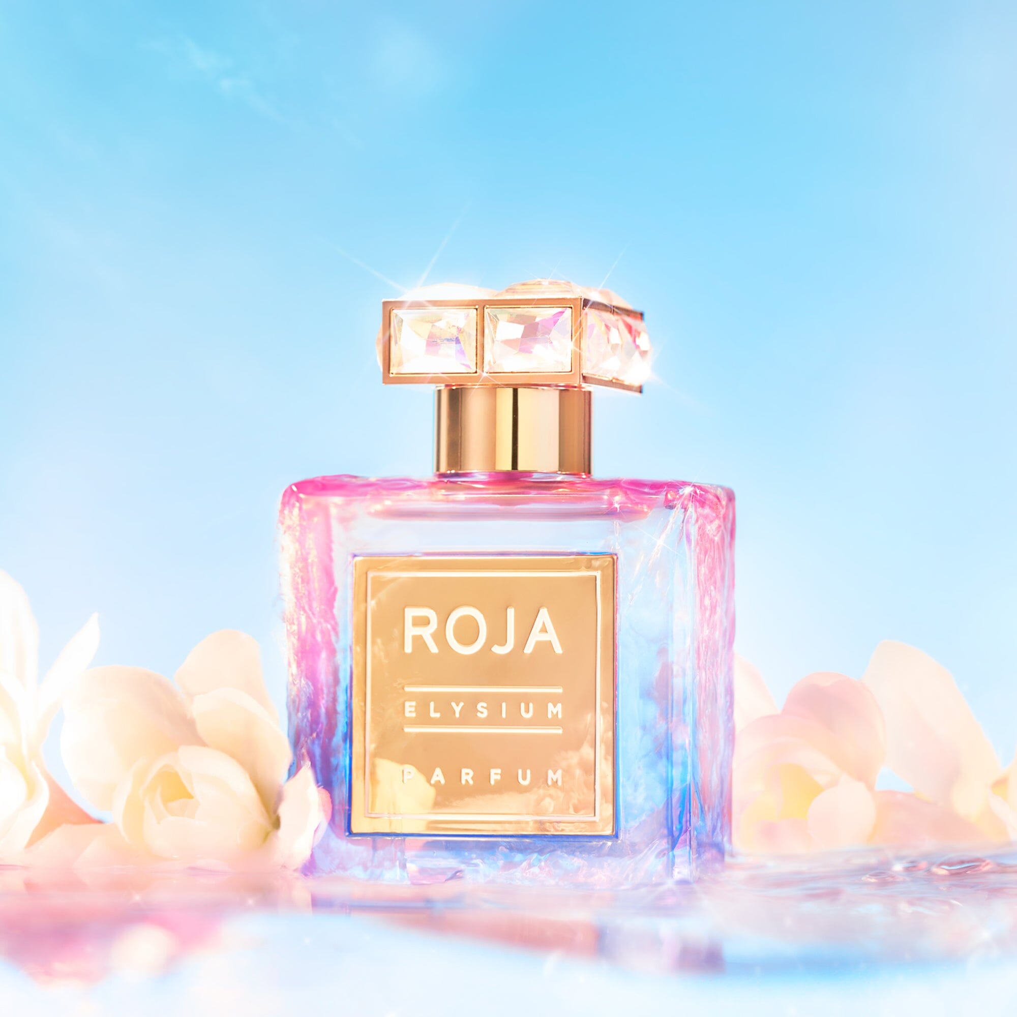 The perfume bottle, labeled Elysium Pour Femme by Roja Parfums, with its jeweled cap, sits among soft white flowers under a bright blue sky. This ethereal blend creates a dreamy and luxurious atmosphere, ideal for invoking the essence of a divine goddess.