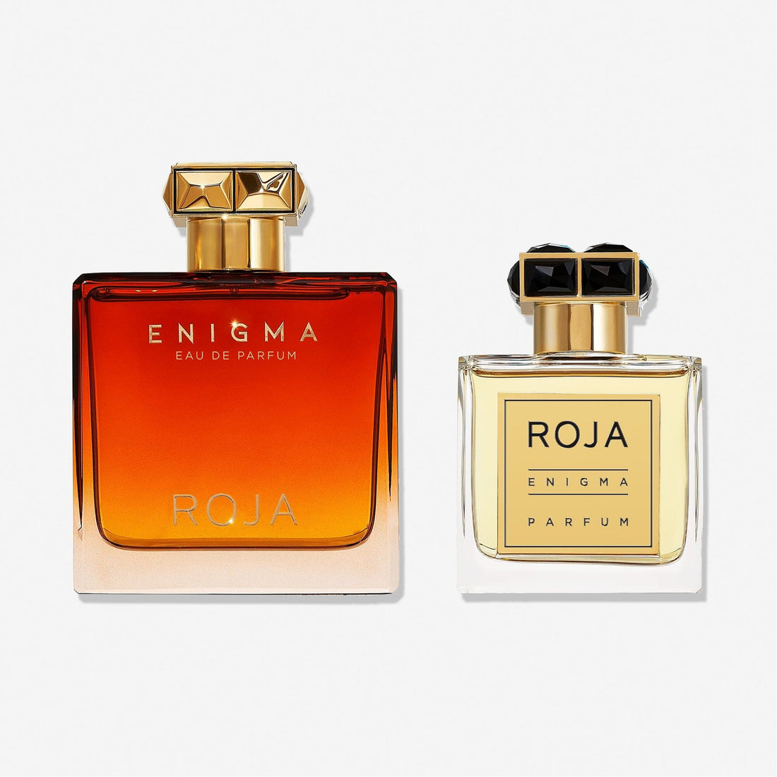The Enigma Gift Set by Roja Parfums includes two ENIGMA POUR HOMME bottles: a larger one with an amber gradient and gold accents, and a smaller clear bottle with gold liquid and a black-topped cap.