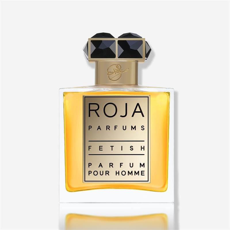 A rectangular bottle of Roja Parfums Fetish Pour Homme, featuring golden accents, a black geometric cap, and amber liquid, suggests a bold leather scent and is shown against a white background.