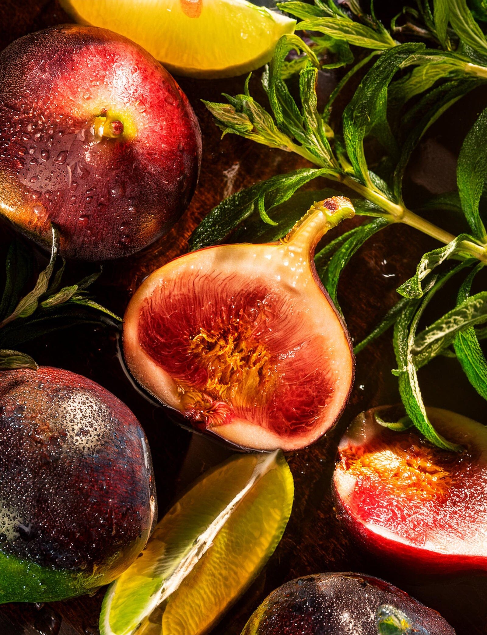 Close-up of fresh figs, herbs, and lemon wedges with water droplets—evoking the complexity and vibrant allure of Fetish Pour Homme by Roja Parfums.
