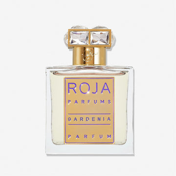 A clear glass perfume bottle with a gold and purple label reading Roja Parfums Gardenia Pour Femme. This elegant white floral scent has a gold cap topped with two large, square, clear gems.