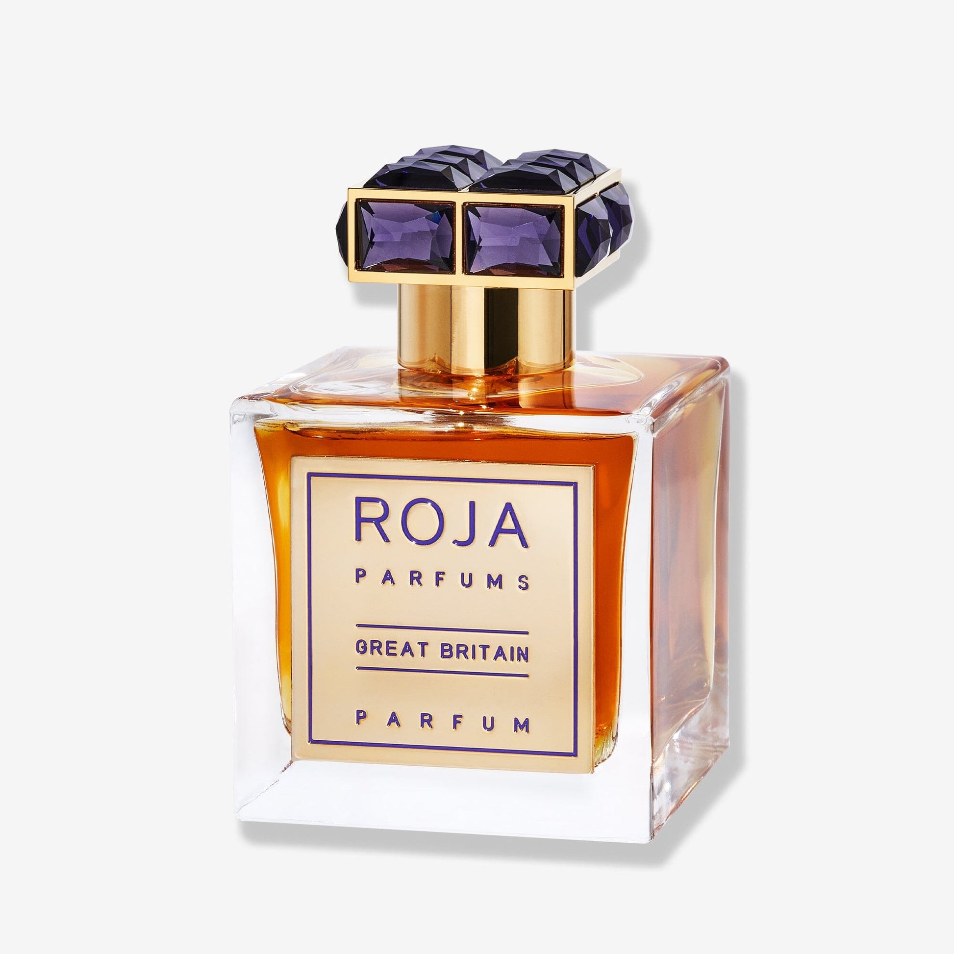 A square glass bottle of Roja Parfums Great Britain, filled with amber liquid and topped with a gold and purple geometric cap, stands against a plain white background, embodying refined British perfumery.