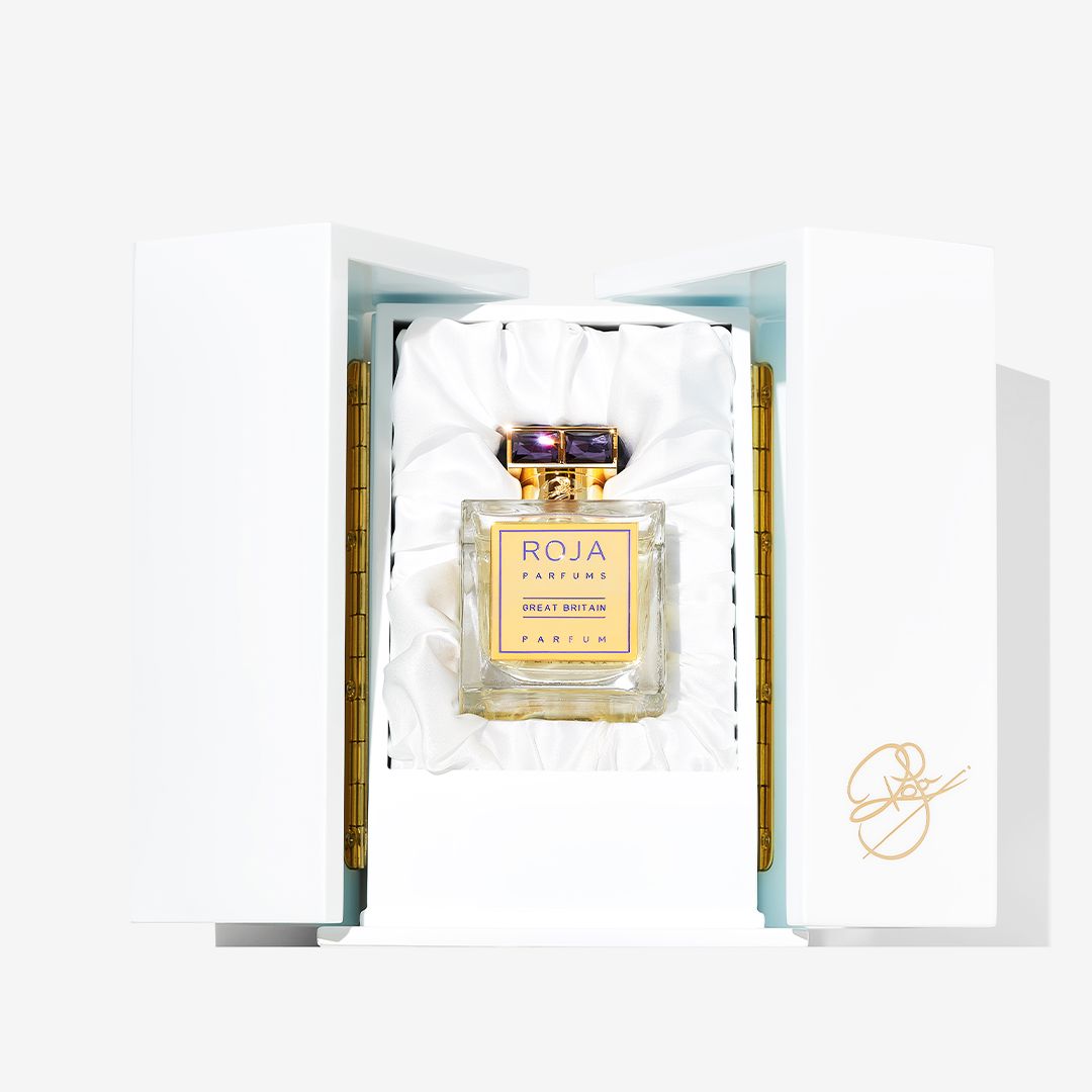 A bottle of Roja Parfums Great Britain stands upright in a white, satin-lined box with gold hinges and a gold signature on the front.