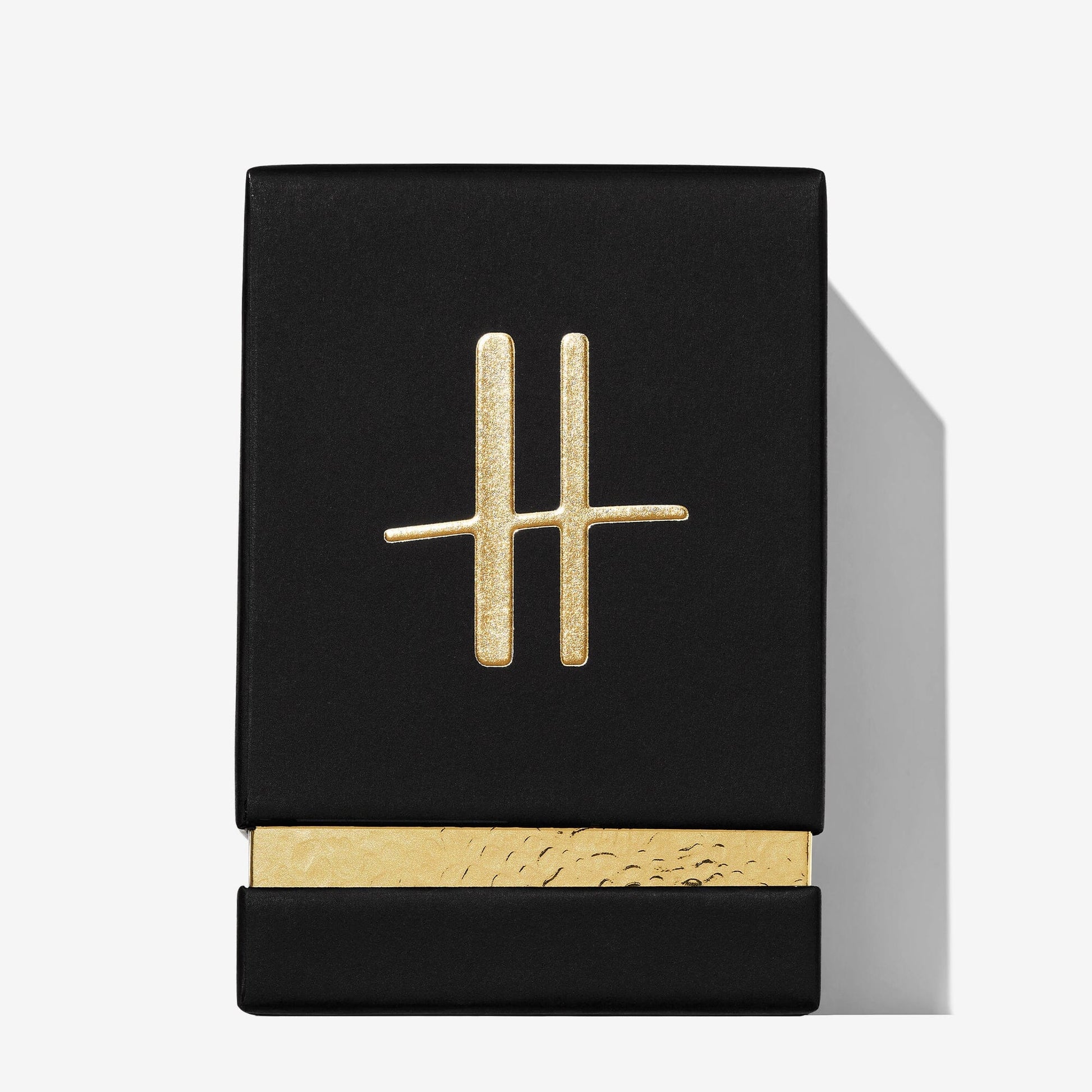 A black rectangular box with a gold metallic H logo on the lid and a gold textured base sets off Roja Parfums’ Harrods Pour Homme—an exclusive men’s luxury perfume—against a light background for an elegant presentation.