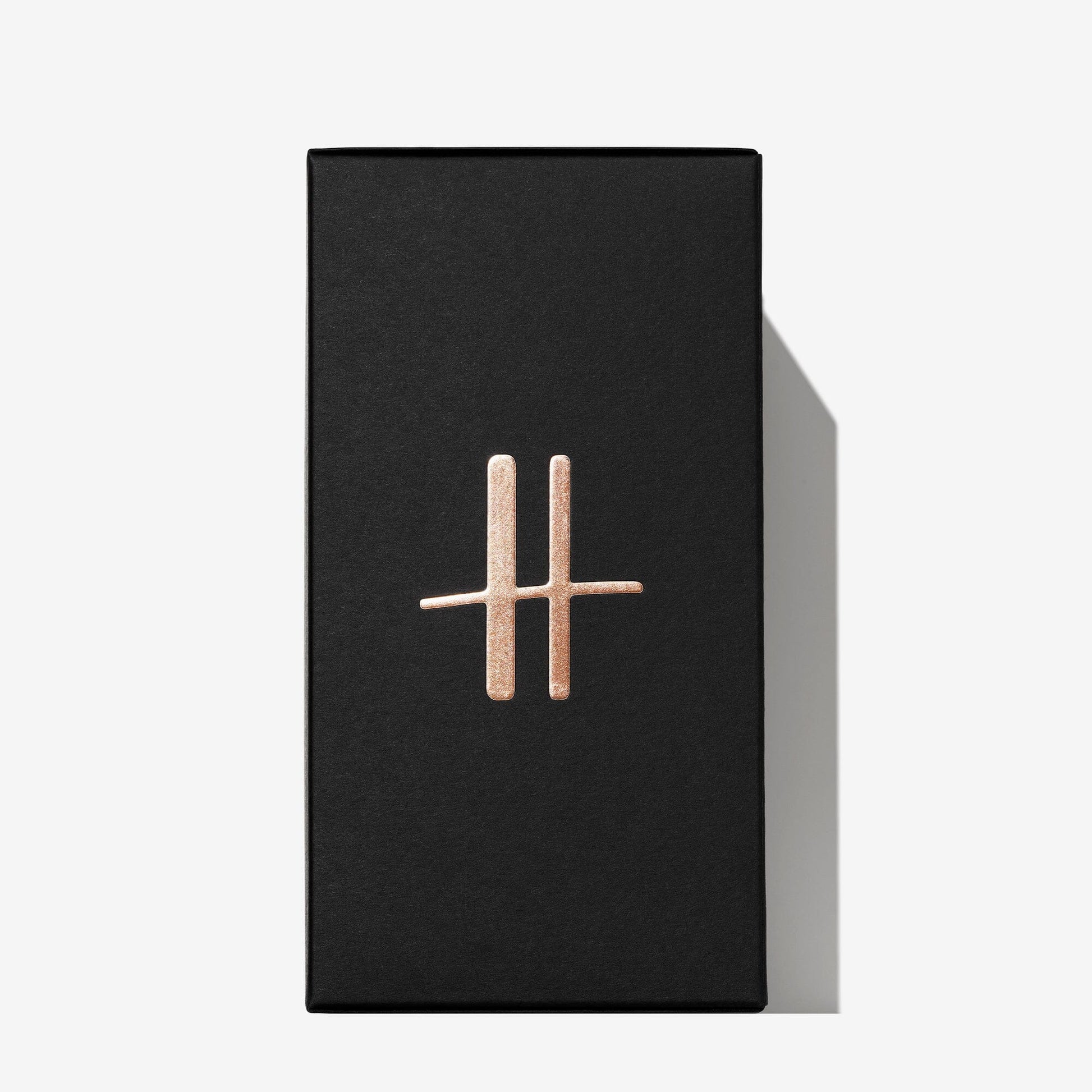 A rectangular black box for Roja Parfums Harrods Black Tier, styled like luxury perfume packaging, displays a metallic gold double-line symbol and casts a rightward shadow on a white background.