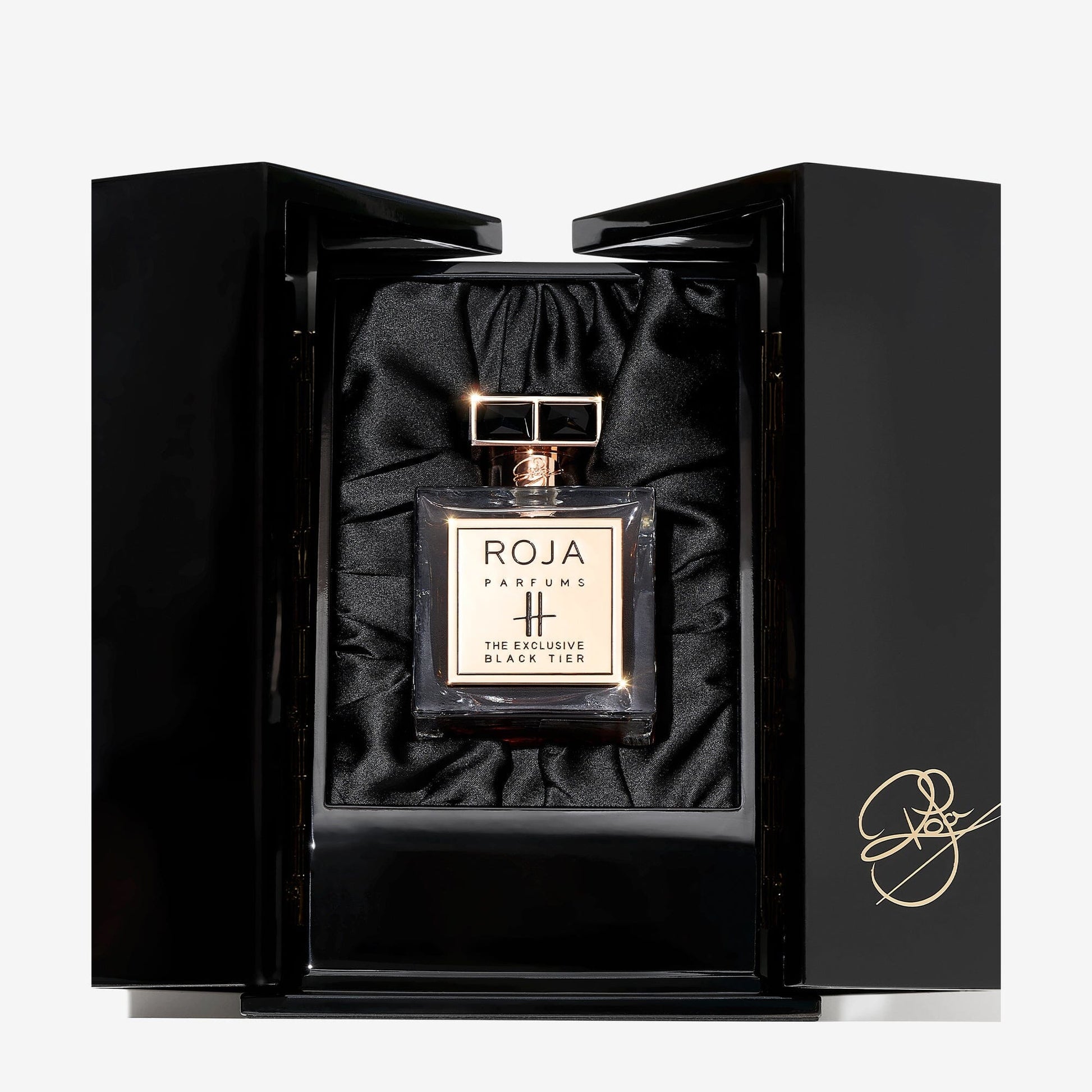 A bottle of Roja Parfums Harrods Black Tier perfume is showcased in an open black box lined with black satin and adorned with a gold signature on the lower right corner.